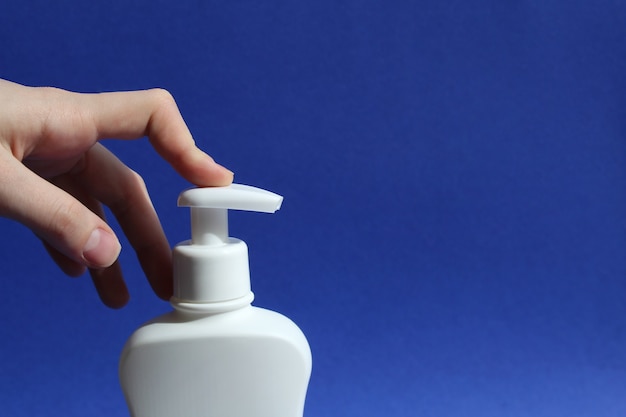 womans finger presses the dispenser of a white bottle of antiseptic on a blue background antibacterial gel with alcohol