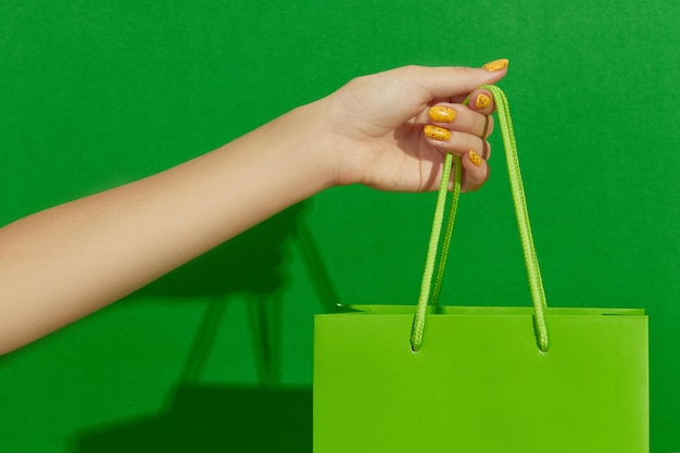 Womans hand holding shopping bag on green background shopping sale concept