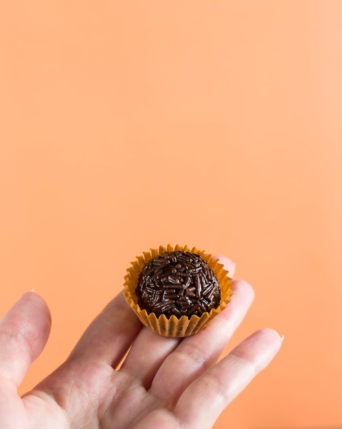 A womans hand holding a vegan brigadeiro Typical Brazilian sweet Orange background