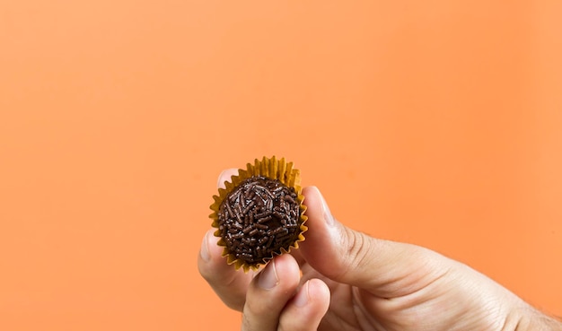 A womans hand holding a vegan brigadeiro Typical Brazilian sweet Orange background