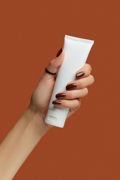 Womans hand holding white tube on brown background self care concept