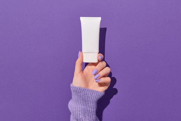 Womans hand holding white tube on violet background skin health care concept