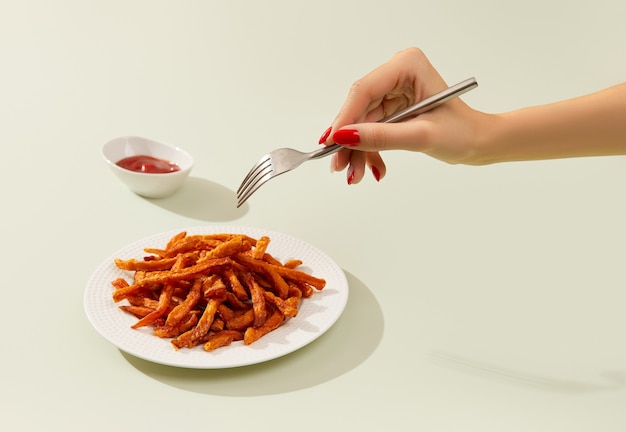 Womans hand takes sweet potato fries on green table