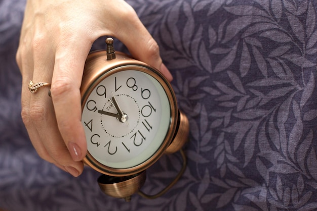 A womans hand with an alarm clock hanging from the bed The concept of a difficult awakening an early rise