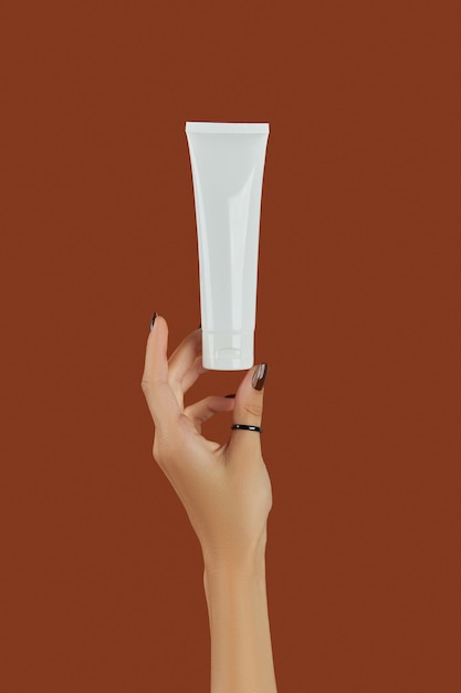 Womans hand with cosmetic cream or cleanser on brown background