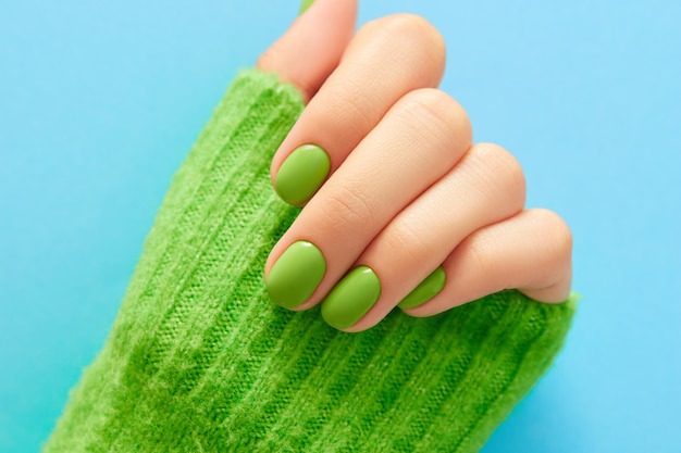 Womans hand with green manicure close up on blue background Beauty treatment spa body care Salon concept