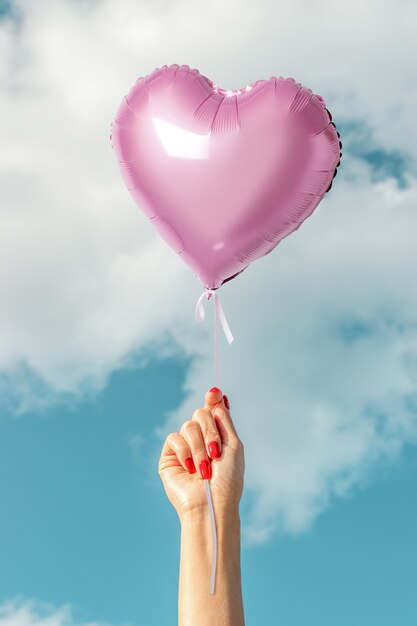 Photo womans hand with pink heart balloon on of sky