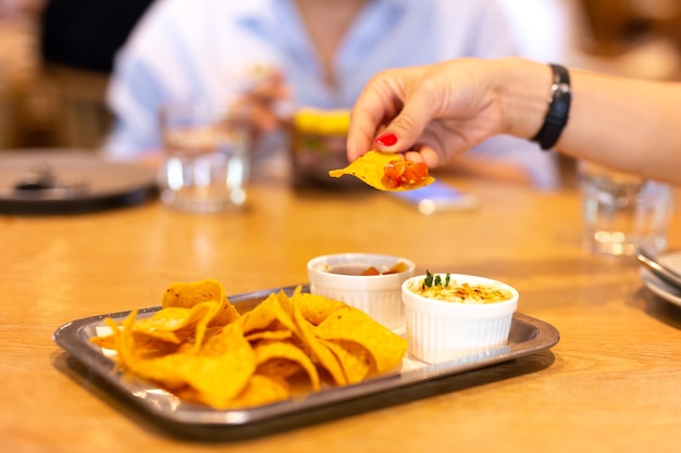 Womans hand with red color nail having a tortilla chip bruschetta sauce at lunch time with