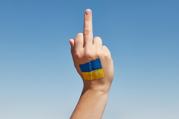 Womans hand with ukrainian flag symbol show fuck sign against the blue sky Stop war