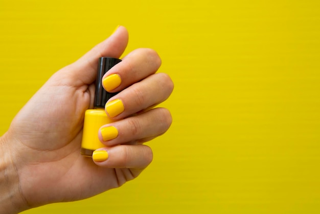 Photo womans hand with yellow nails holding a bottle of nail polish