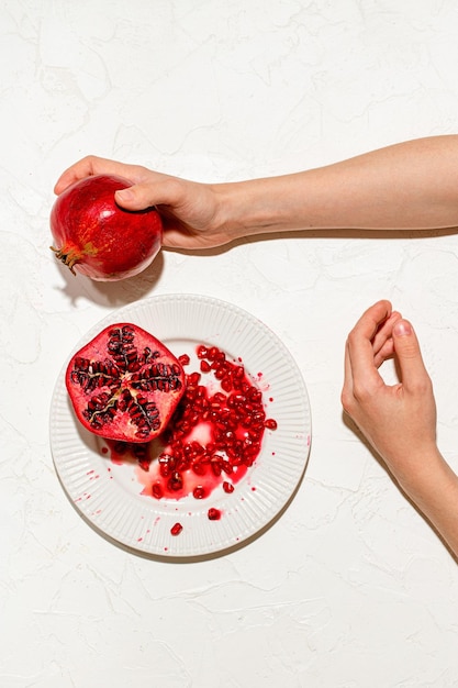 The womans hands are holding a ripe pomegranate on a white table and a sliced juicy pomegranate is l