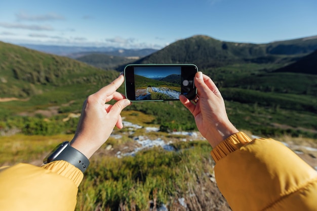 A womans hands close up making panoramic photo of green mountains using smartphone