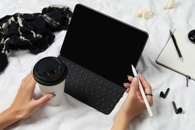 Womans hands holding black tablet with blank screen on a white bed mockup template