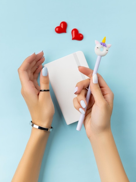 Womans hands holding notepad over blue table Female summer accessories