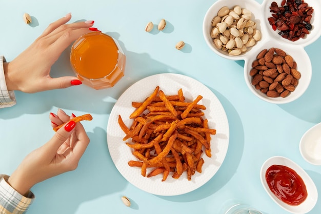 Womans hands take sweet potato fries nuts and drinks on blue background with long shadows in minimal