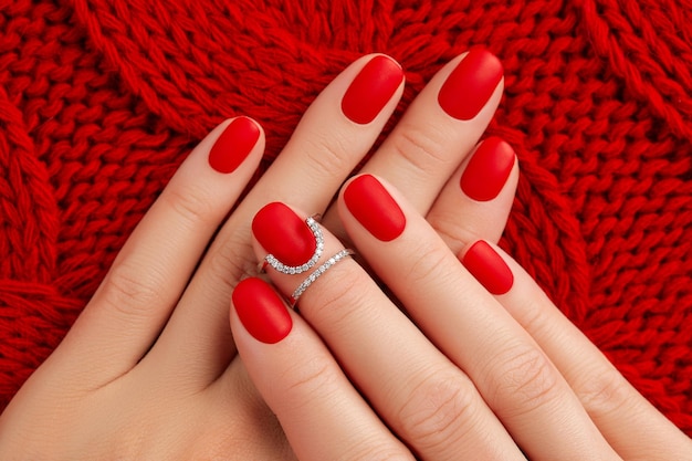 Womans hands with matt manicure on red knitted coverlet Winter manicure pedicure design trends