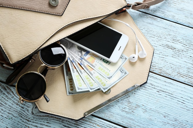 Photo womans purse with glasses phone and money on light blue wooden background