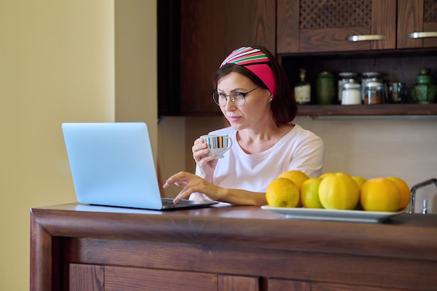 Women 40s age resting at home with a cup of coffee looking at laptop