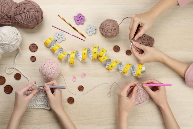 Women crocheting with threads at wooden table top view