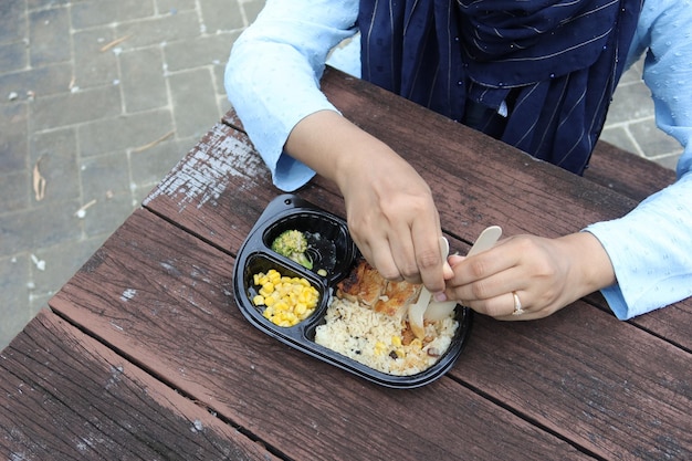 Women eating chicken rice in a take away packet in park bench