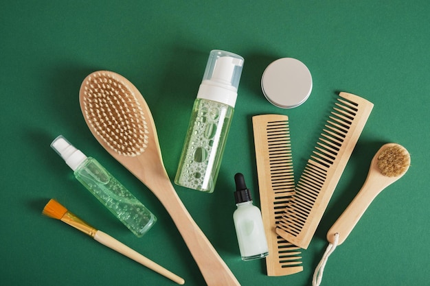 Women hair care set Comb wooden brush gel jar dropper bottle on green background top view