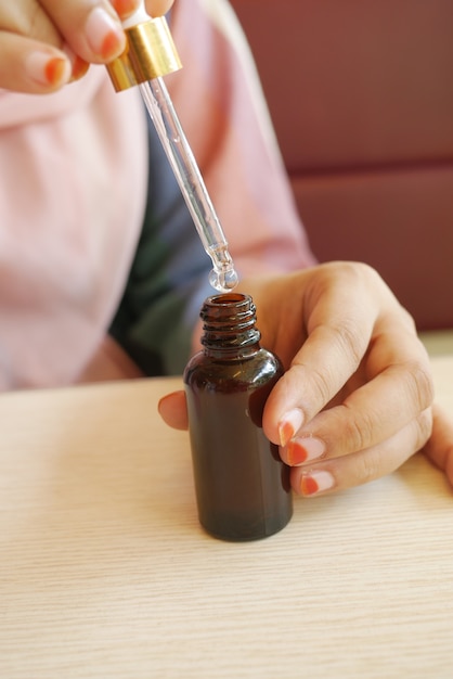 Women hand drop falls from a pipette into a cosmetic bottle