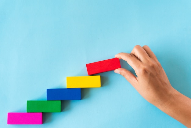 Women hand put red wooden block on colorful wooden blocks in the shape of a staircase