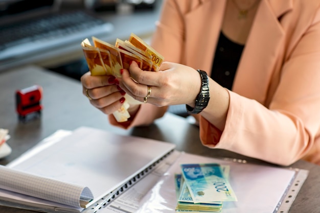 Women Hands holding a fan of money of Israeli New Shekels. Stack of Money scattered on the table. Cropped image of Hand holds banknotes. Selective focus. Money background. Financial concept