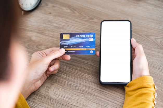 Women hands holding Mobile Phone with blank screen and Credit Card on office desk and using mobile phone for Online Shopping, Internet Banking, Online Trading