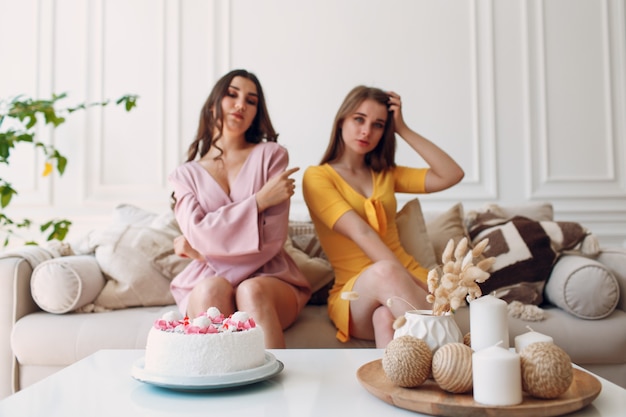 Women happy friends at home sitting and smiling with white birthday cake.