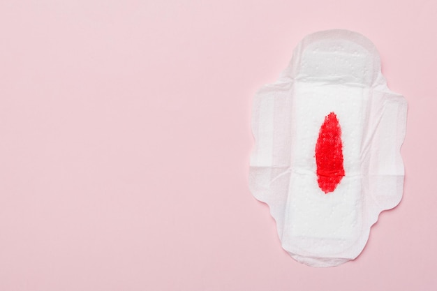 Women hygiene products or Sanitary pad with red feather on colored background Pastel color Closeup Empty place for text Female daily hygiene