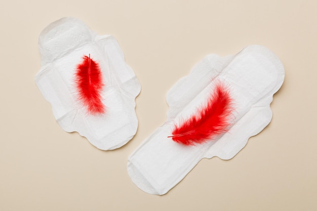 Women hygiene products or Sanitary pad with red feather on colored background Pastel color Closeup Empty place for text Female daily hygiene