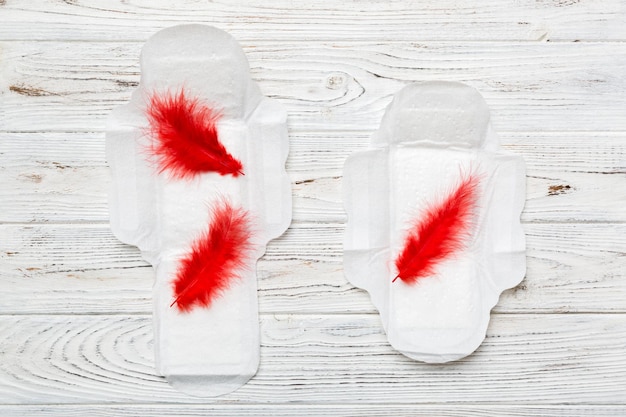 Women hygiene products or Sanitary pad with red feather on colored background Pastel color Closeup Empty place for text Female daily hygiene