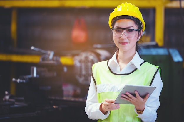 Women industrial plant with a tablet in hand, Engineer looking of working at industrial machinery setup in factory.