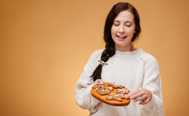 Women joyfully hold a wooden board with gingerbread christmas cookies decorated with icing