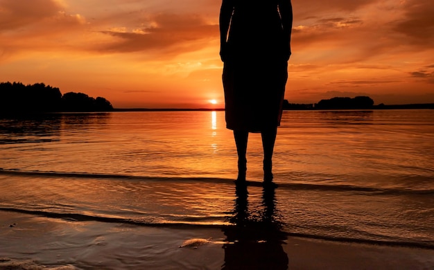 Women legs feet silhouette standing in water at sunset over lake