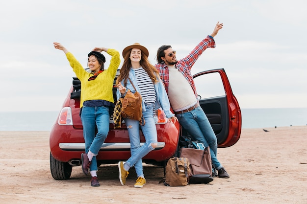 Women and man with upped hands near car on beach