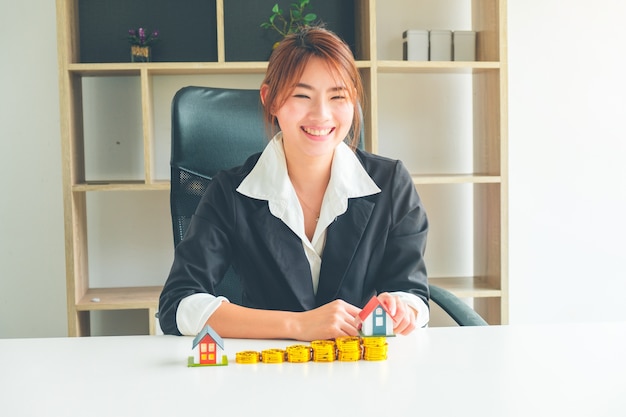 Women Real Estate Agent hold a small house model in her hand and gold coin stack 