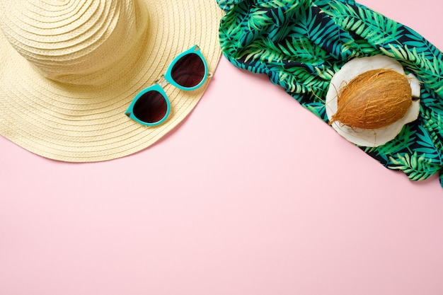 Women's beach accessories: straw hat, sunglasses, coconut, green scarf on pink background. Traveler stuff concept, summer background with copy space.