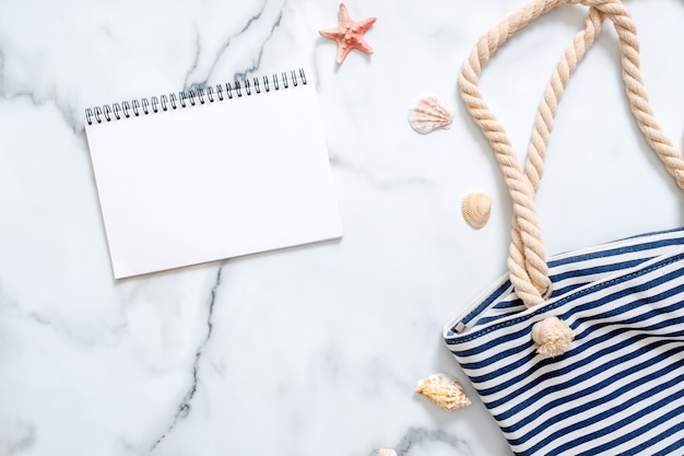 Women's desk with striped beach bag, seashells and blank notepad.