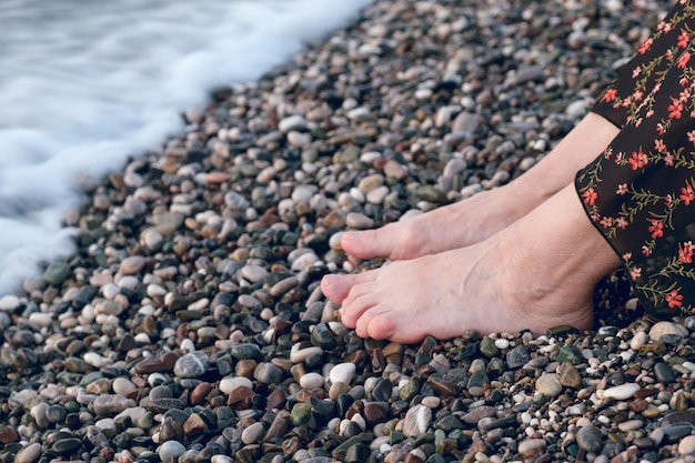 Women's feet at the water's edge on a pebble beach