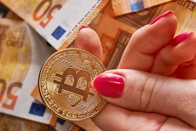 Women's hand with bitcoin and 50 fifty euros of background bills banknotes