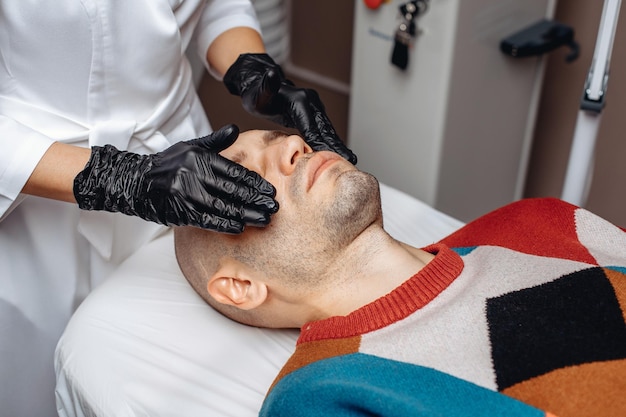 Women's hands of a cosmetologist in gloves moisturize the man's skin with a special cream for skin care procedures