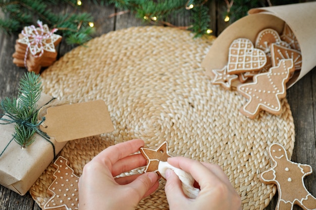 Women's hands decorate Christmas gingerbread cookies with sugar frosting on beautiful wooden.