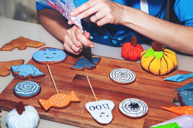 Women's hands decorate gingerbread as a sweet Halloween gift for children