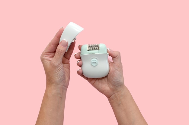 Women's hands hold a blue epilator in their hands On a pink background