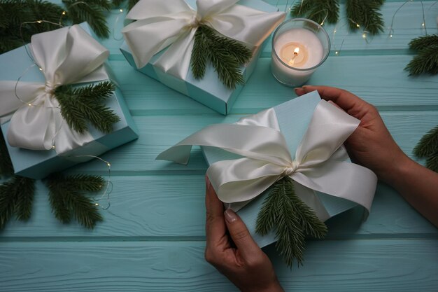 Women's hands hold a gift. There are gifts on the table and a candle is burning.