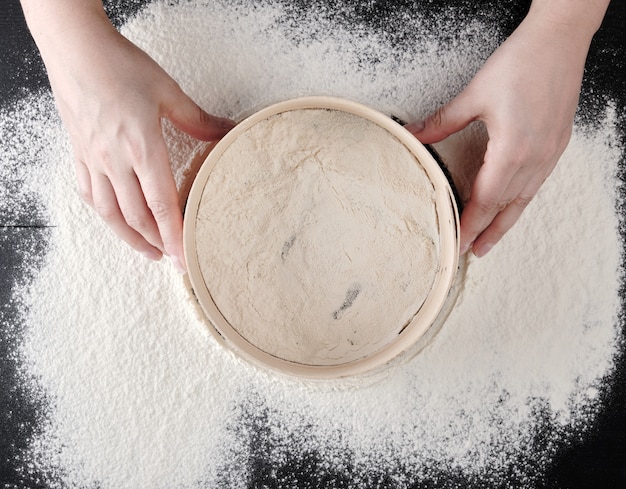 Women's hands hold a round wooden sieve and sift white wheat flour