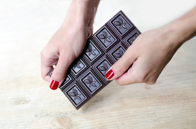 Women's hands hold a whole bar of chocolate. 