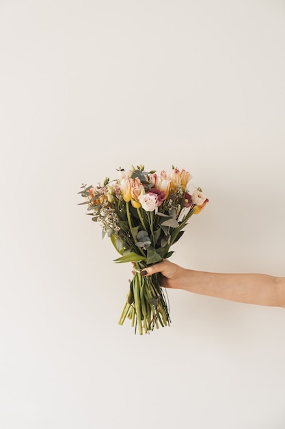 Women's hands holding flower bouquet against white wall